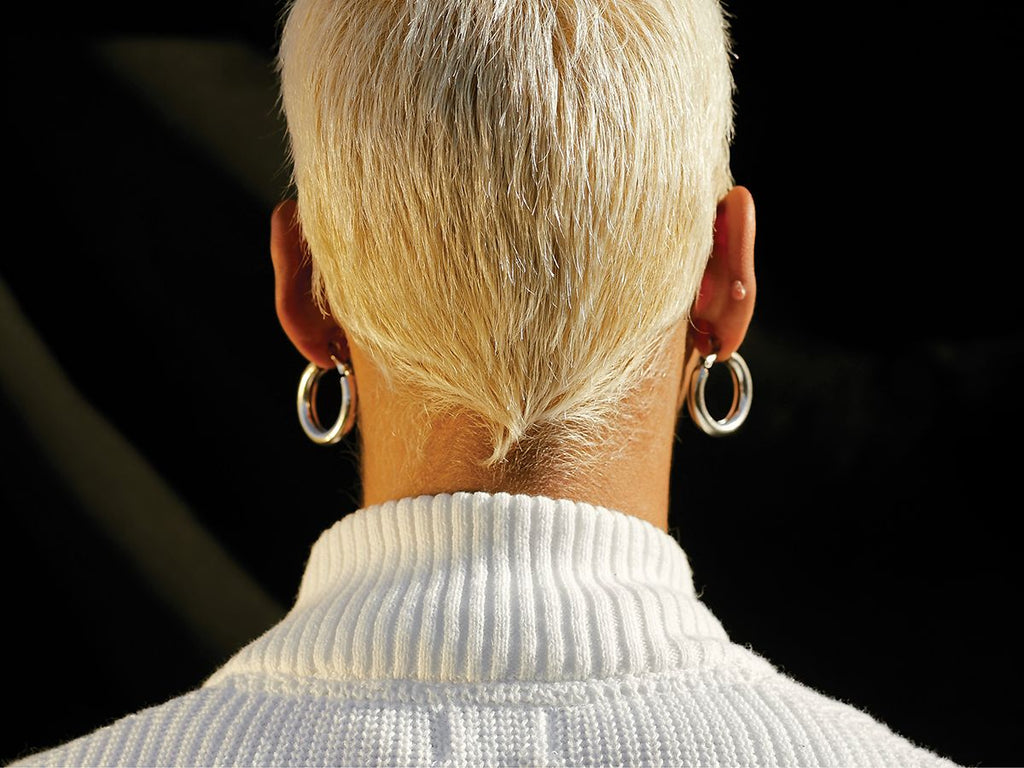 Foto af models baghoved og nakke med kort blondt hår og sølvøreringe.
