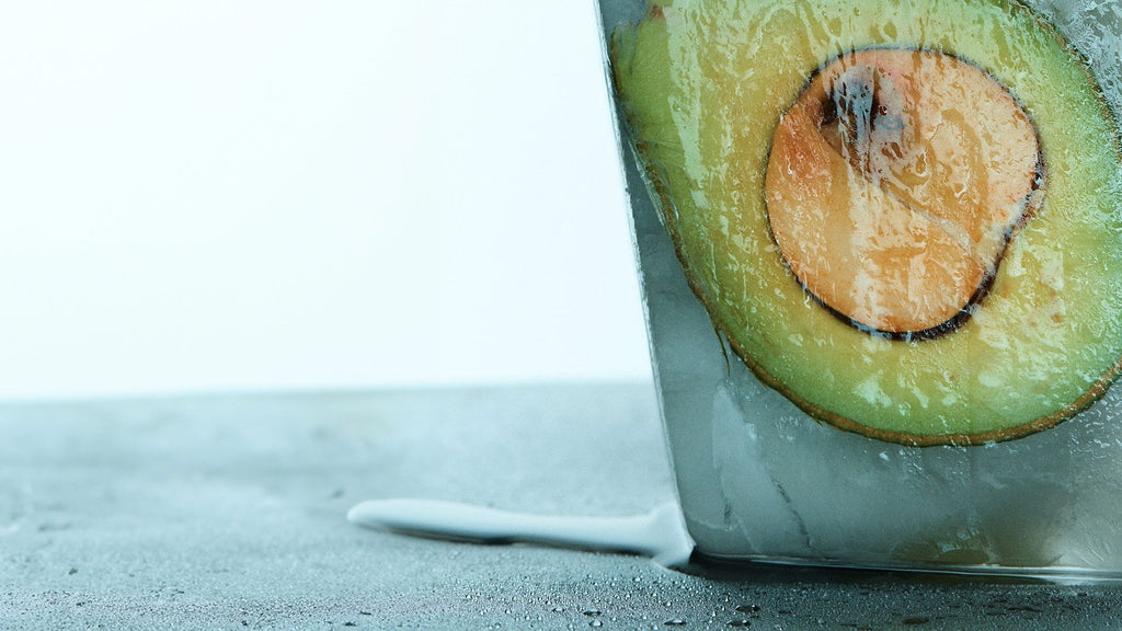 Foto af en avocado – skåret ud i halve – omgivet af smeltende is på et bord.
